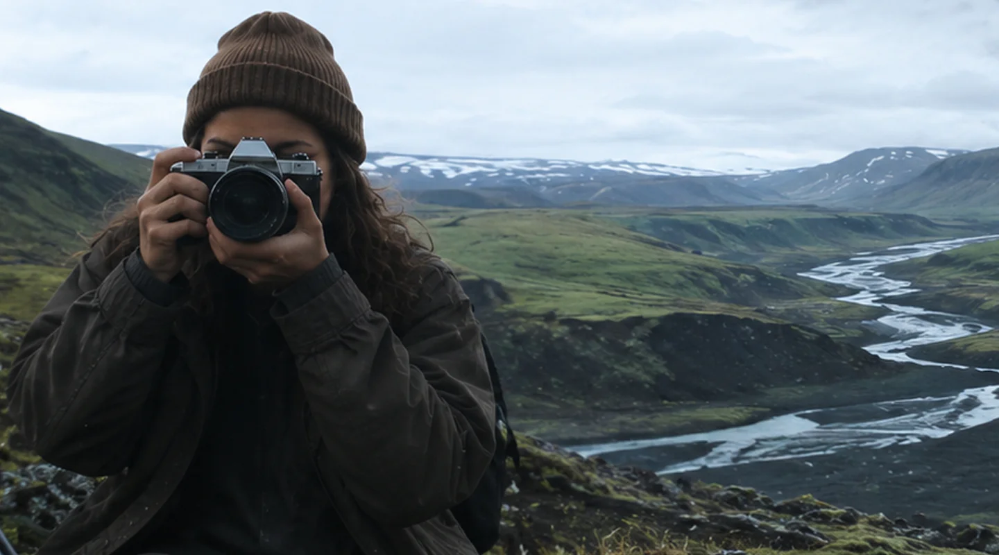 A traveller raising a camera over a glacial river valley